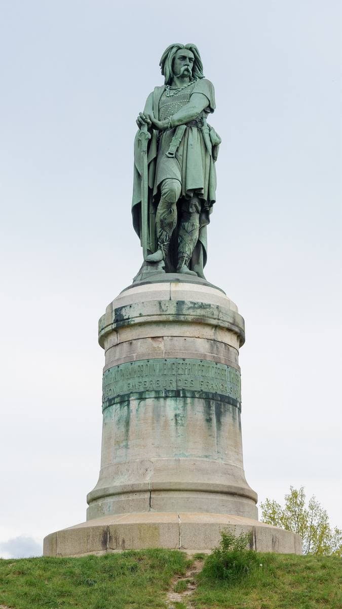 A tall bronze statue of a long-haired Gaulish chief on a high stone plinth
