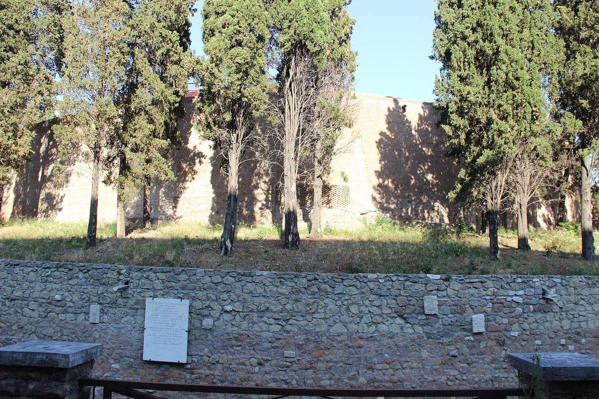 Grassy circular walls of a huge round tomb seen behind a railing