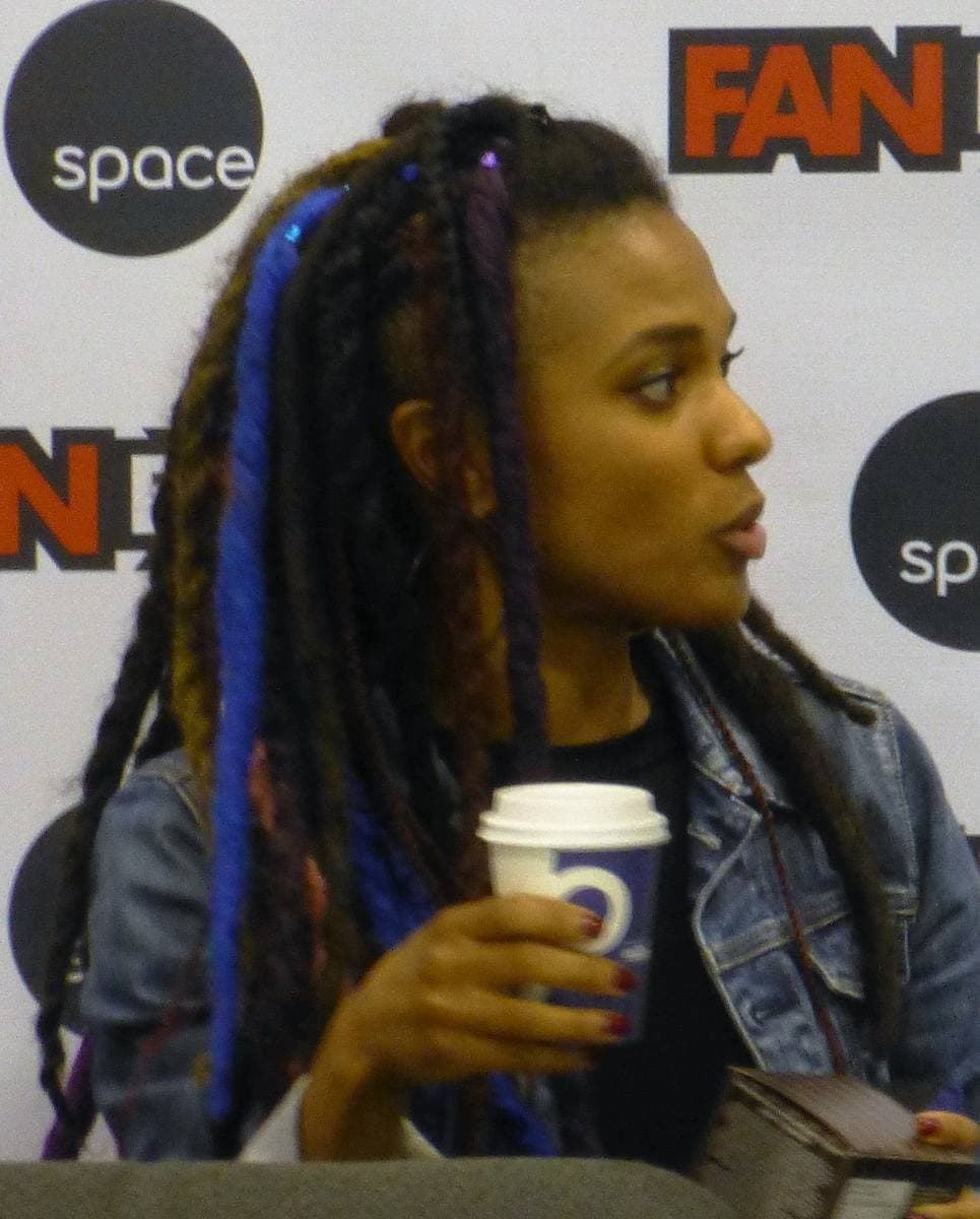 Freema Agyeman with long braids, holding a coffee cup at a convention