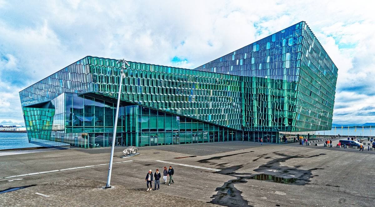 A concert hall clad in green and blue glass panels by the sea