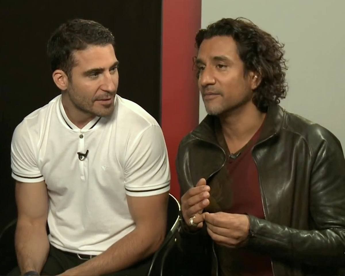 Miguel Ángel Silvestre in a white polo shirt and Naveen Andrews in a leather jacket, seated side by side