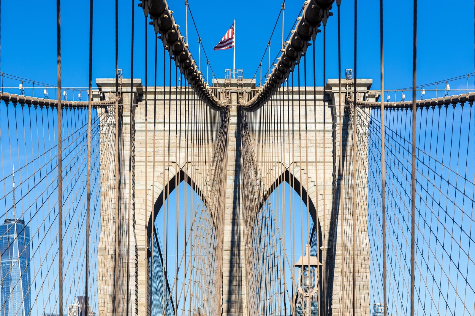 The granite gothic arches of a Brooklyn Bridge tower and its cables against a blue sky