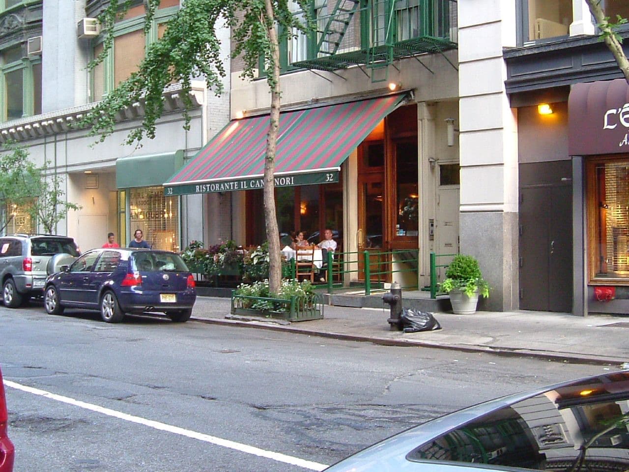 A restaurant awning and potted plants on a tree-lined street