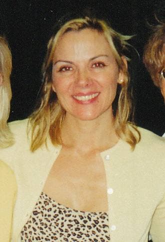 Kim Cattrall, blonde, smiling, in a cream cardigan over a leopard-print top