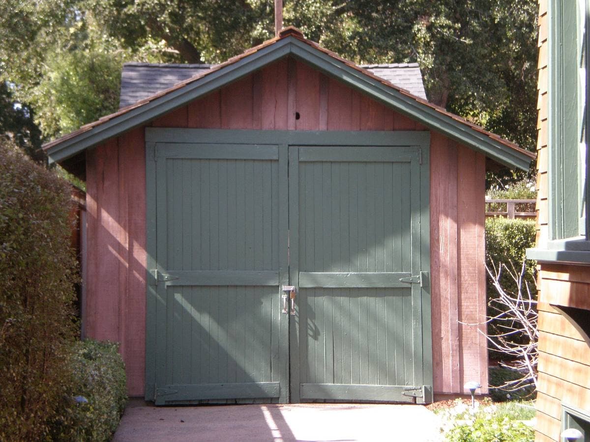 A small wooden one-car garage at the end of a driveway