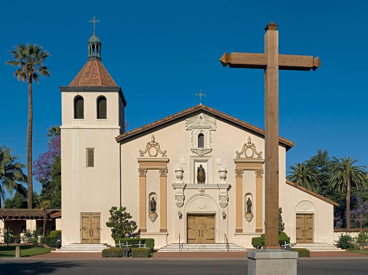 A white mission church with a bell tower behind a rose garden