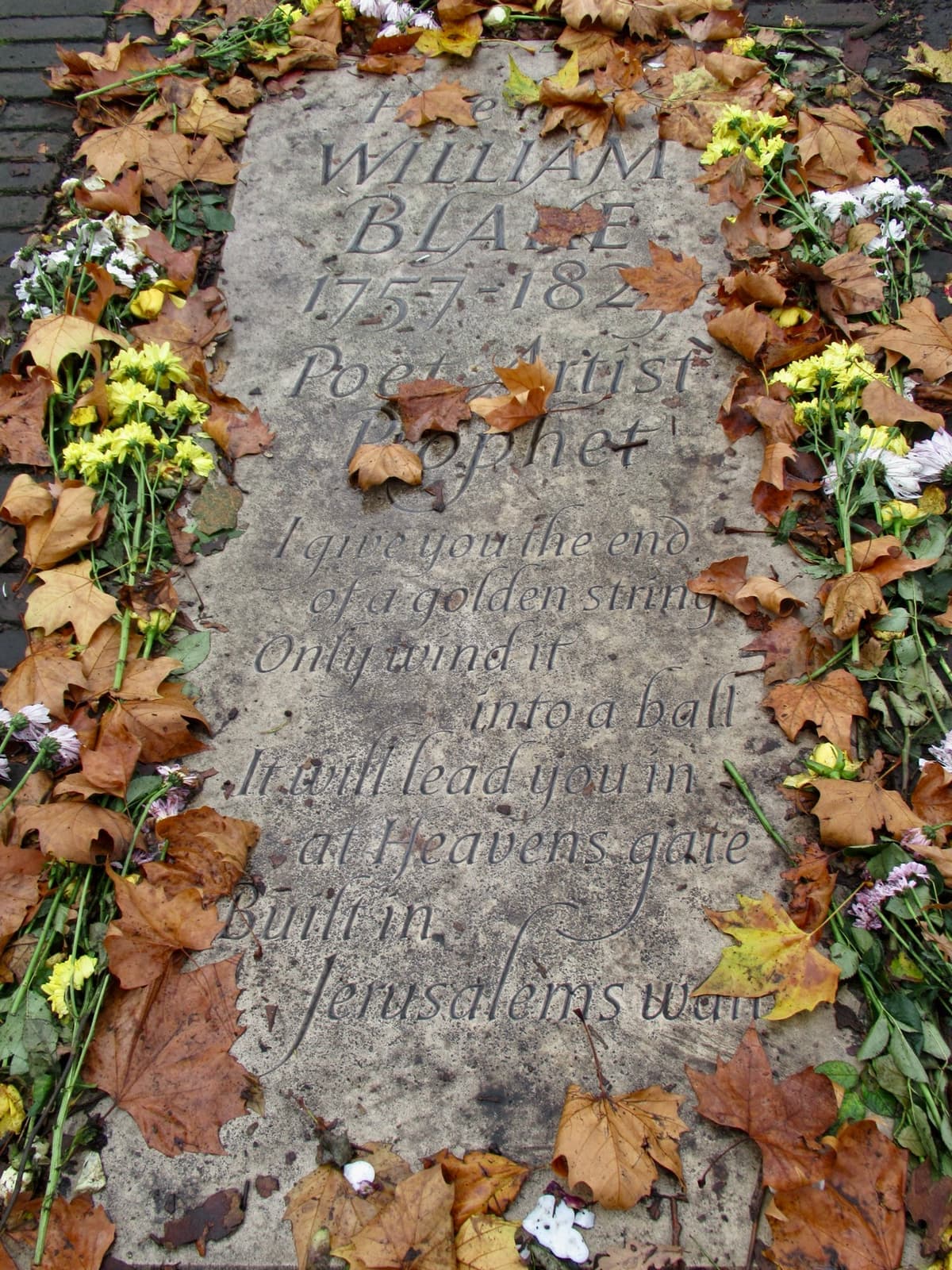 A flat stone slab carved with William Blake’s name, ringed by flowers and leaves