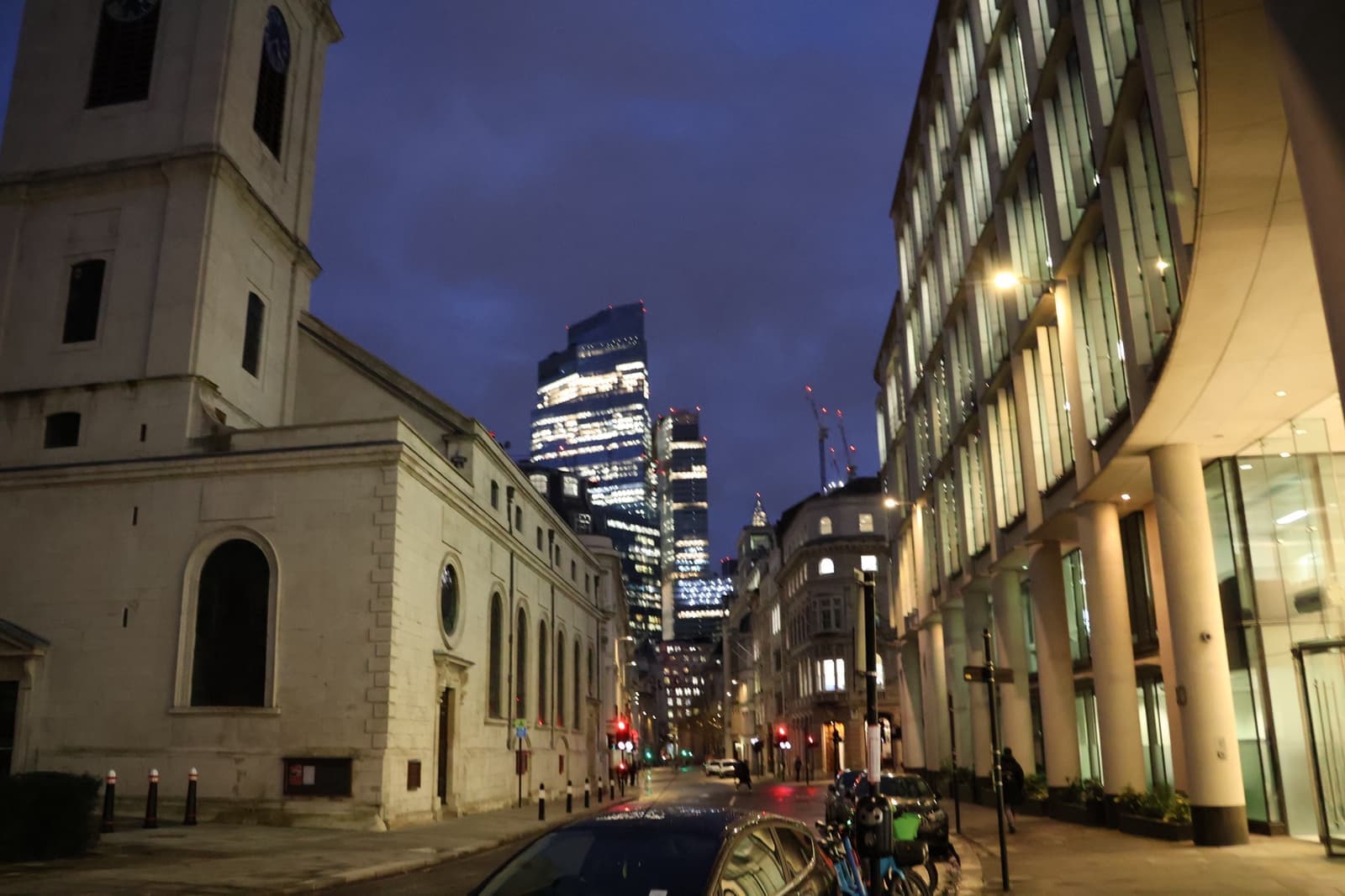 Gresham Street at dusk, a pale stone building on the left and lit office buildings beyond