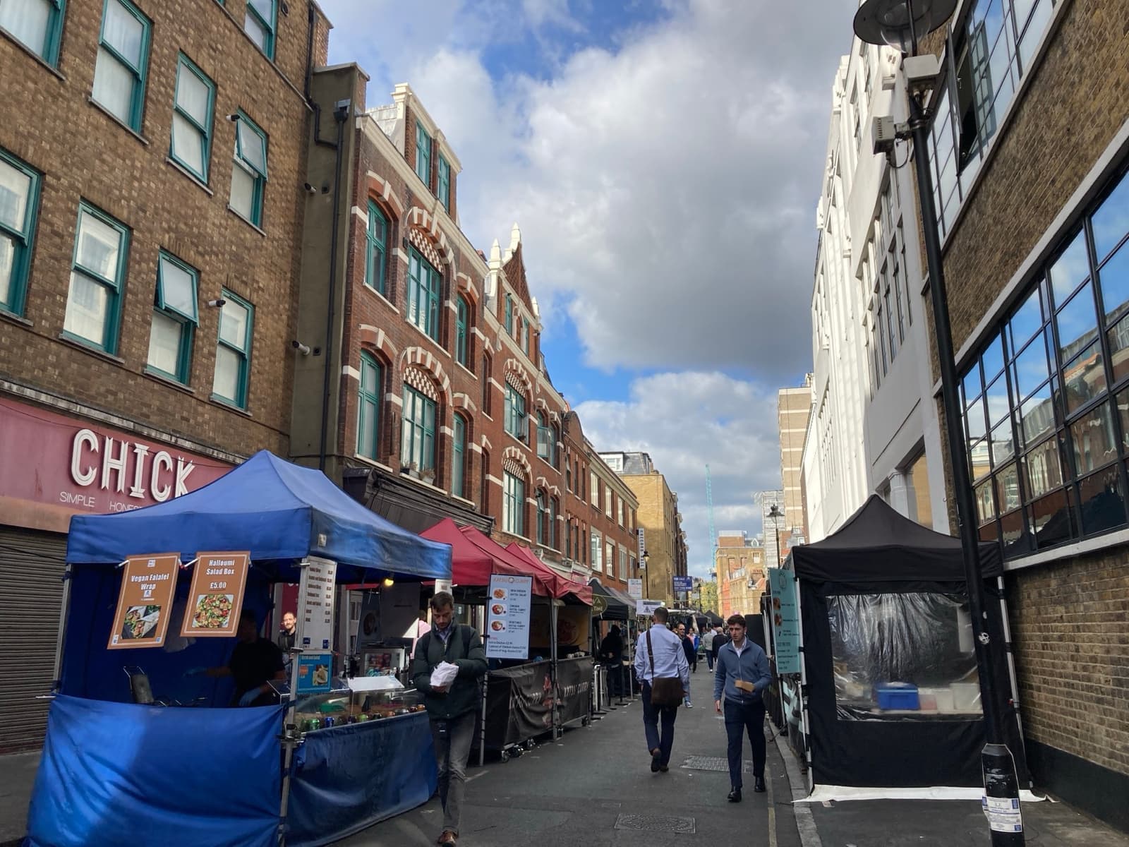 Street-food stalls with blue awnings down a narrow lane of brick buildings
