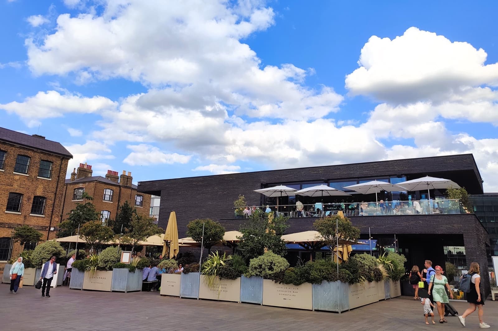 A modern three-storey pub with terraces and umbrellas on a busy square