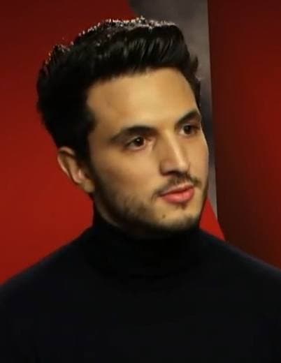 Giacomo Ferrara in a black roll-neck, dark hair swept up