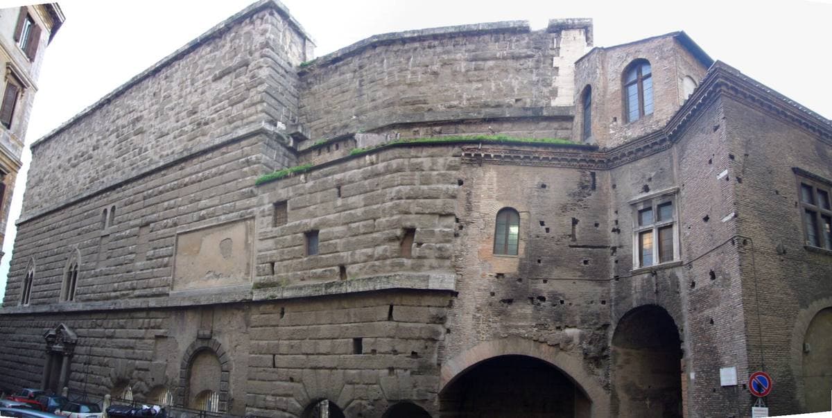 A towering wall of grey stone blocks with a later building on top