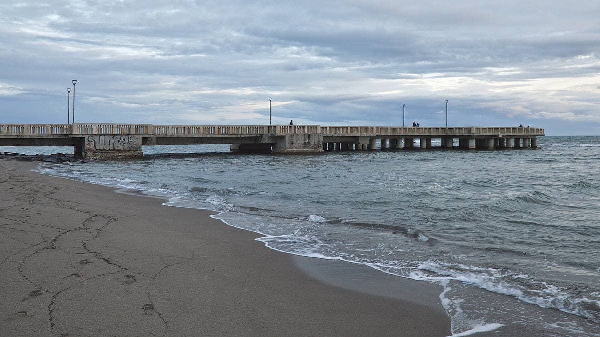 A long concrete pier running out into a calm sea at dusk