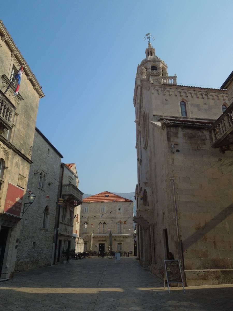 The stone bell tower of St Mark’s Cathedral over a small paved square in Korčula