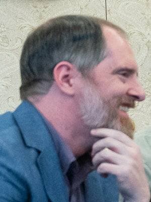 Brendan Hunt, bearded, in a suit