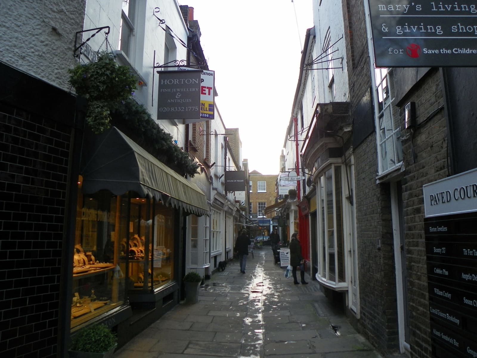 A narrow paved lane of small shopfronts and hanging signs between old brick buildings
