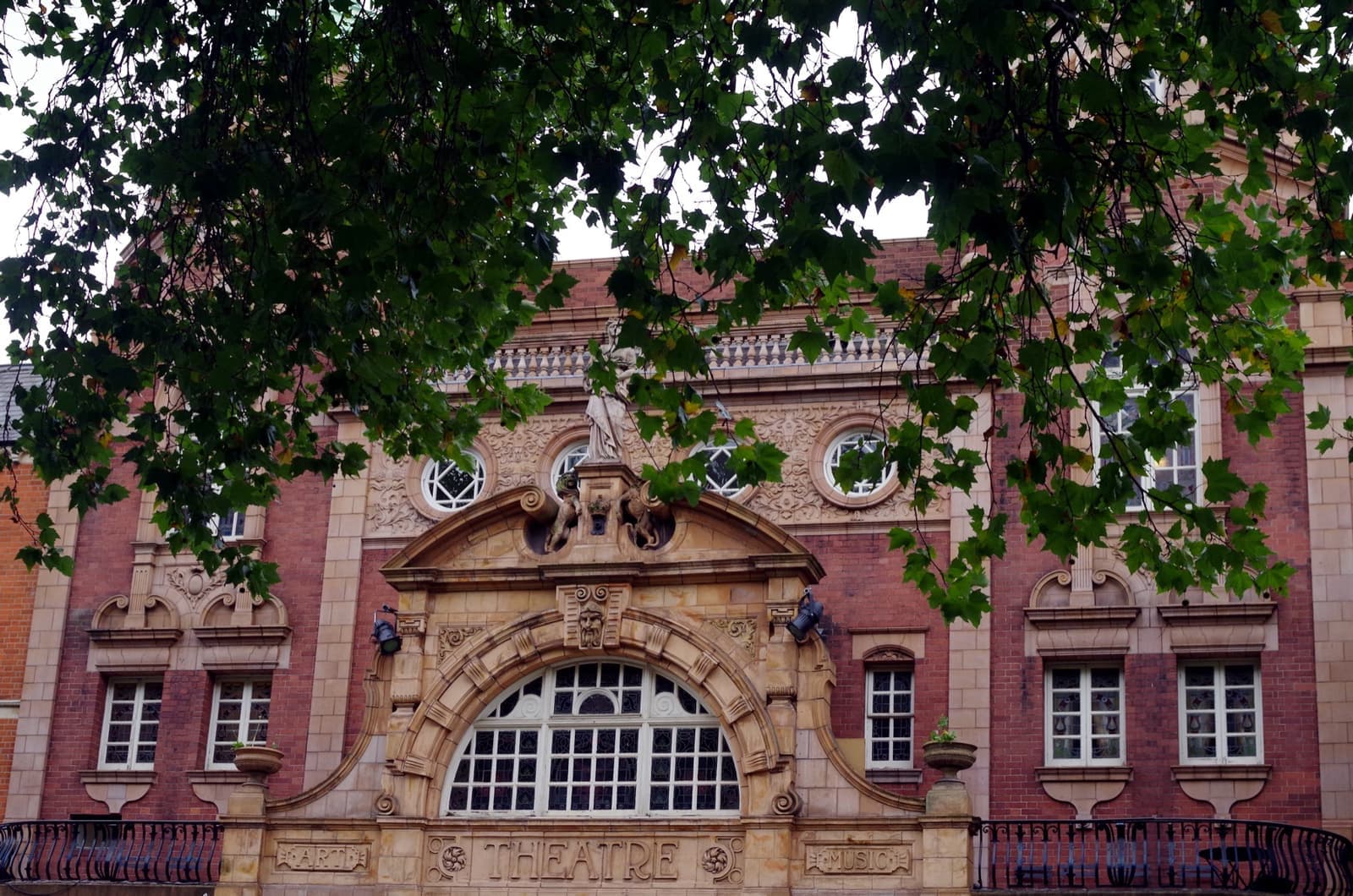 The ornate red-brick and terracotta front of a Victorian theatre seen through leaves
