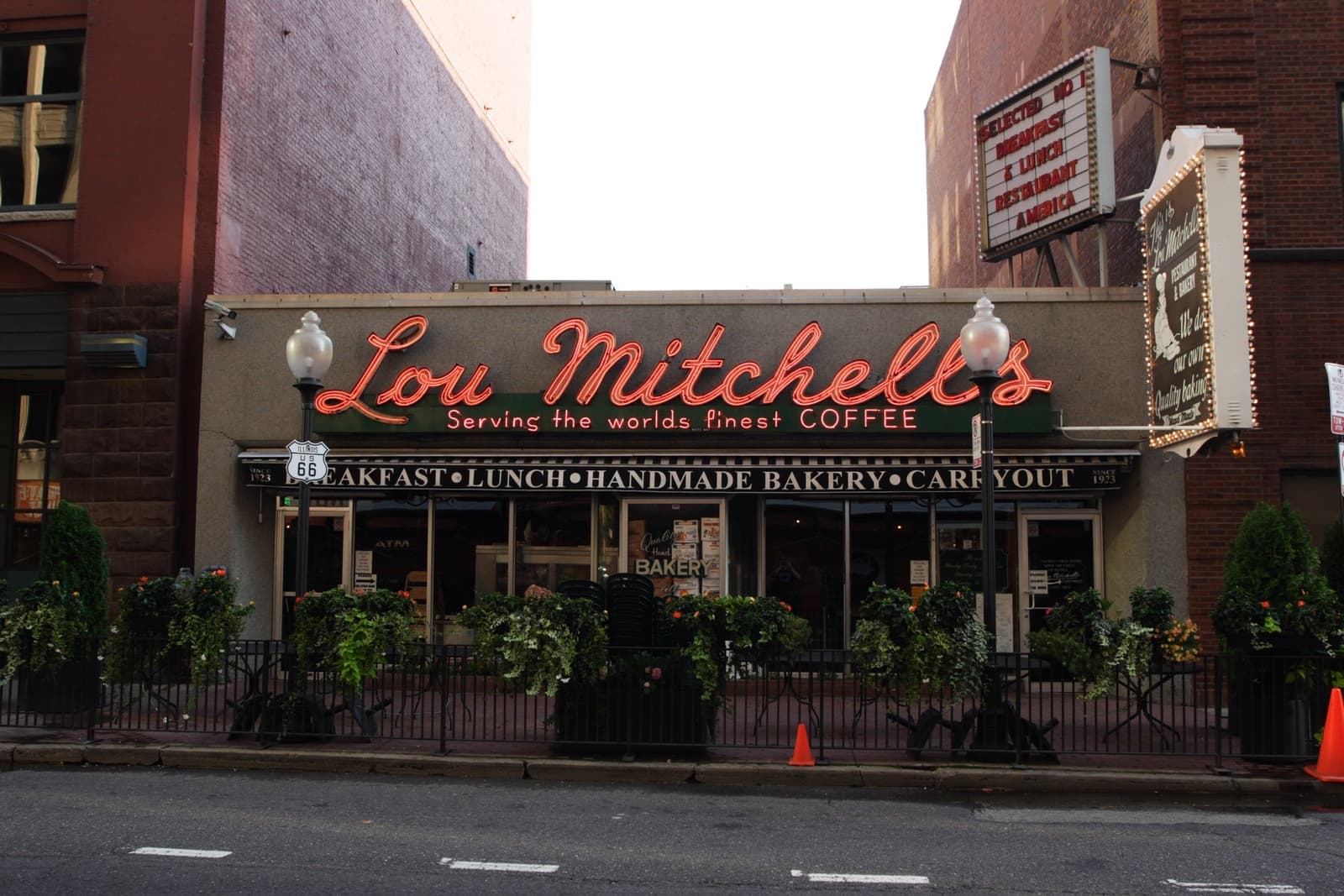 A diner front with a red script sign, globe lamps and a vertical sign above the door