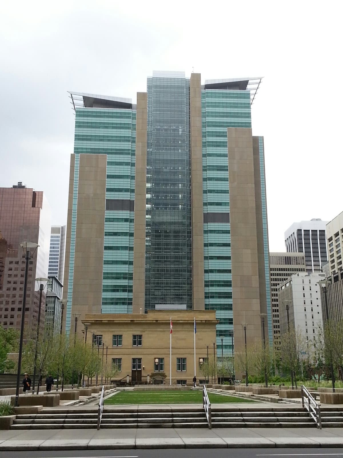 Green glass court towers rising behind an older sandstone courthouse and a lawn