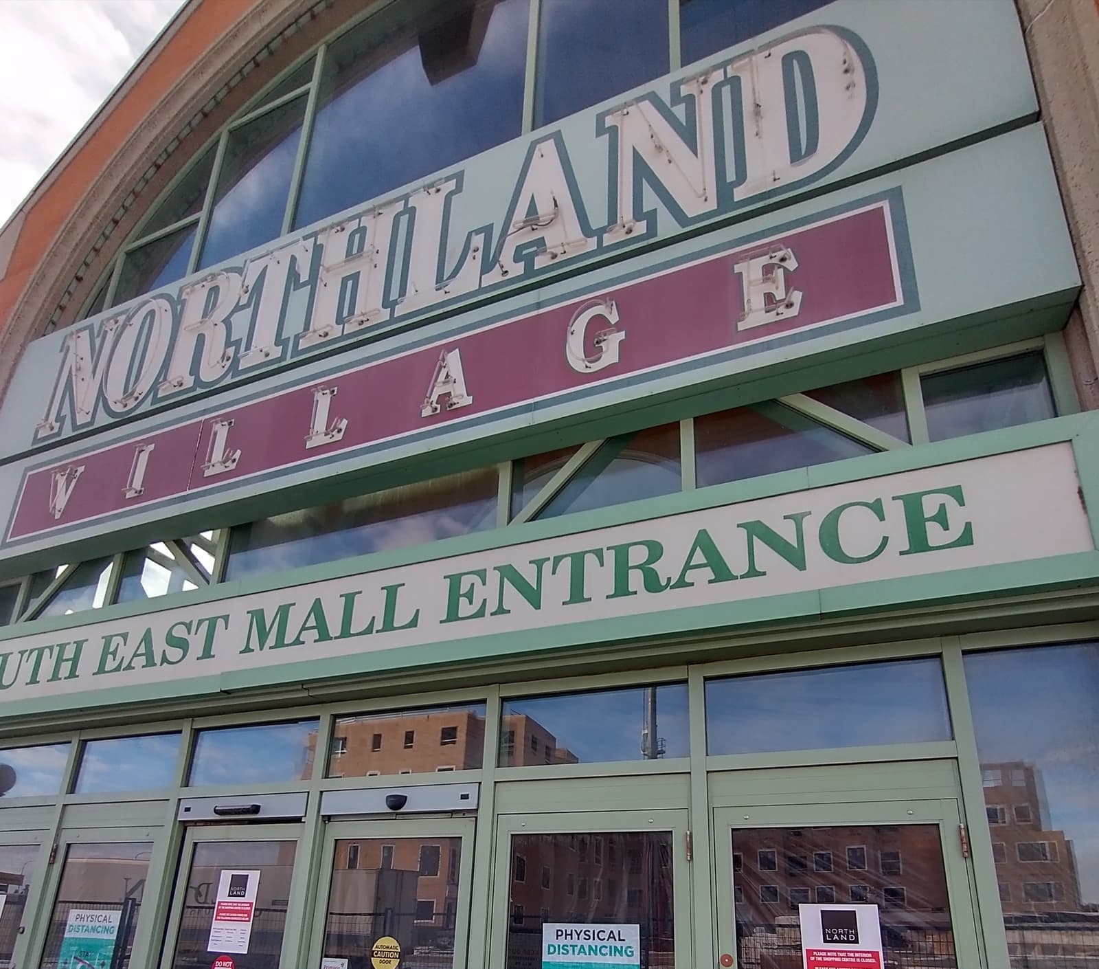 A faded mall entrance sign reading Northland Village above dark glass doors