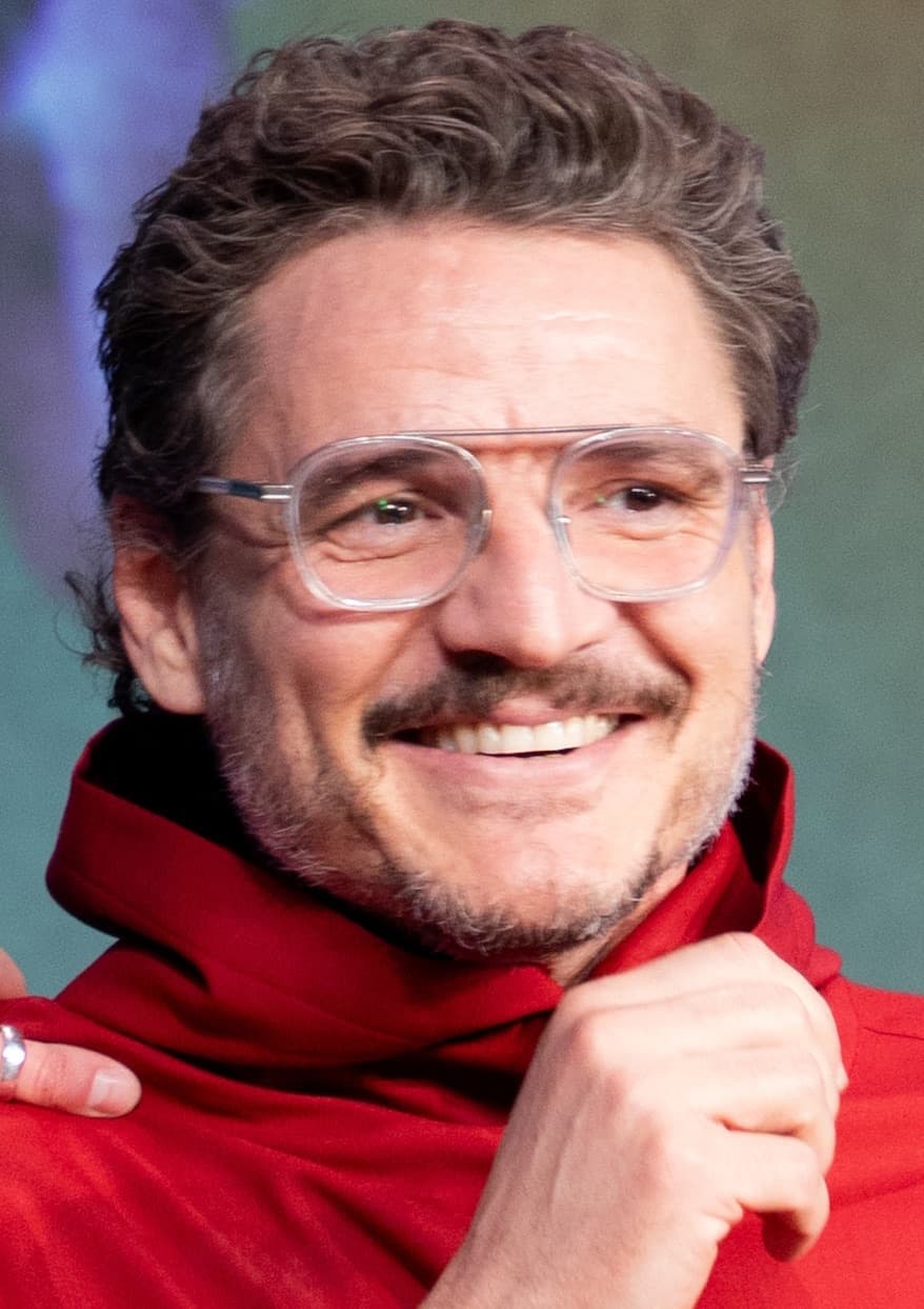 Pedro Pascal smiling in glasses and a red jacket