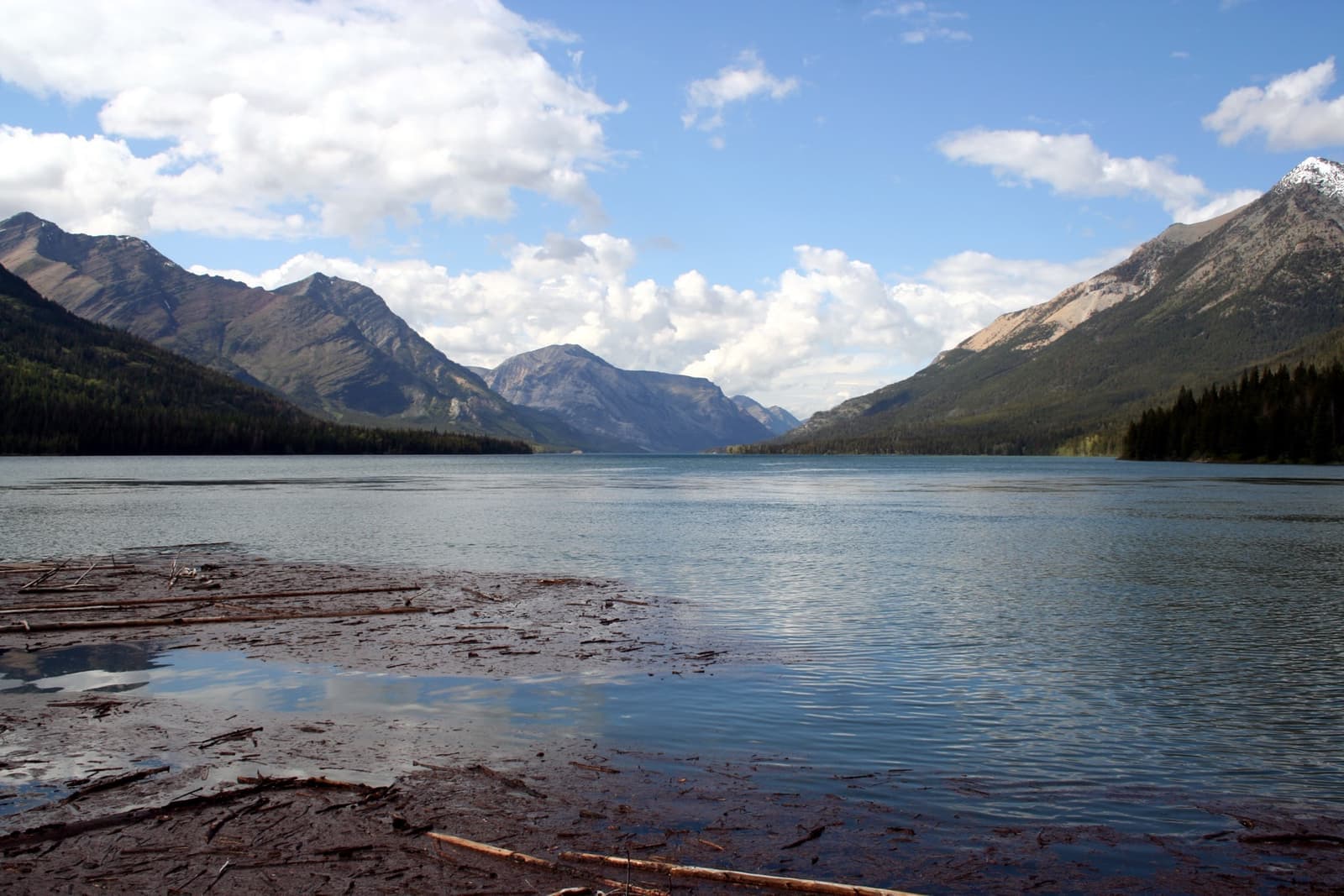 A long blue lake between steep forested mountains under scattered cloud