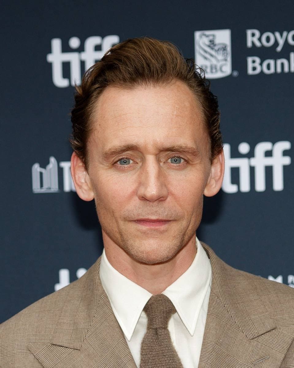 Tom Hiddleston smiling, in a dark suit