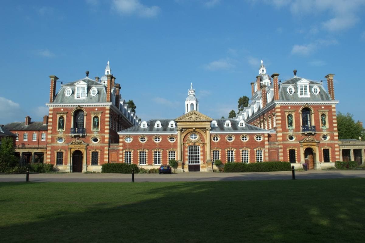 A long red-brick and stone building with towers behind a lawn