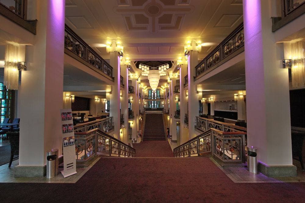 A theatre foyer with coloured glass panels and a curving balcony