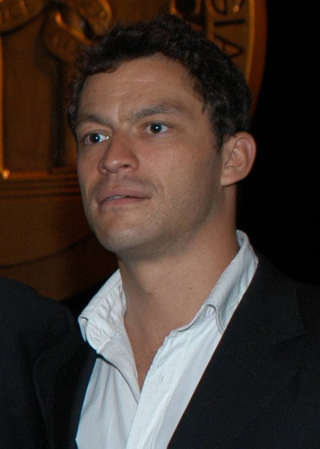 Dominic West in a dark jacket and open white shirt, smiling