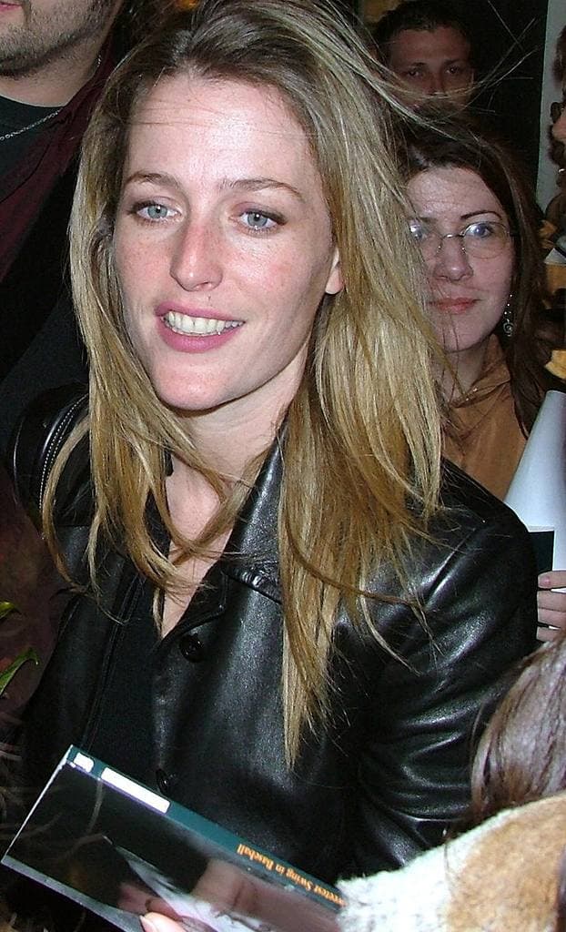 Gillian Anderson with long fair hair and a black leather jacket, smiling