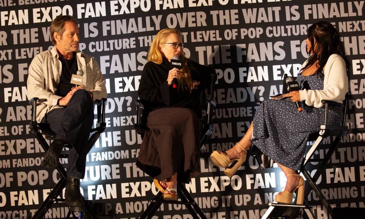 David Duchovny and Gillian Anderson seated on stage in director’s chairs, holding microphones, with a host beside them
