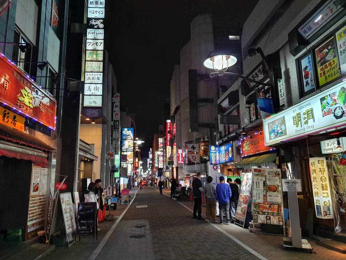 A narrow nightlife street at night, lit shop signs on both sides