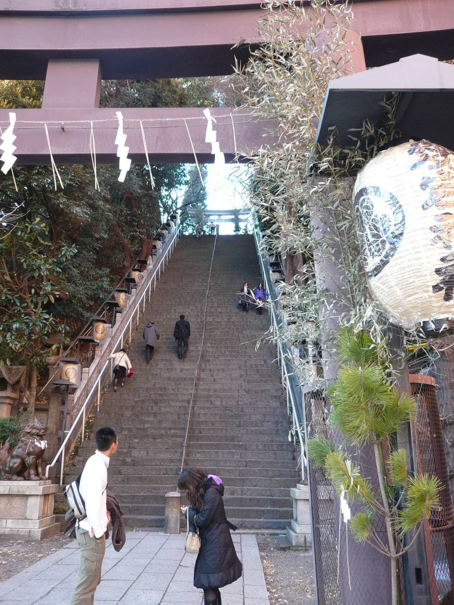 A very steep stone staircase climbing between trees to a red gate