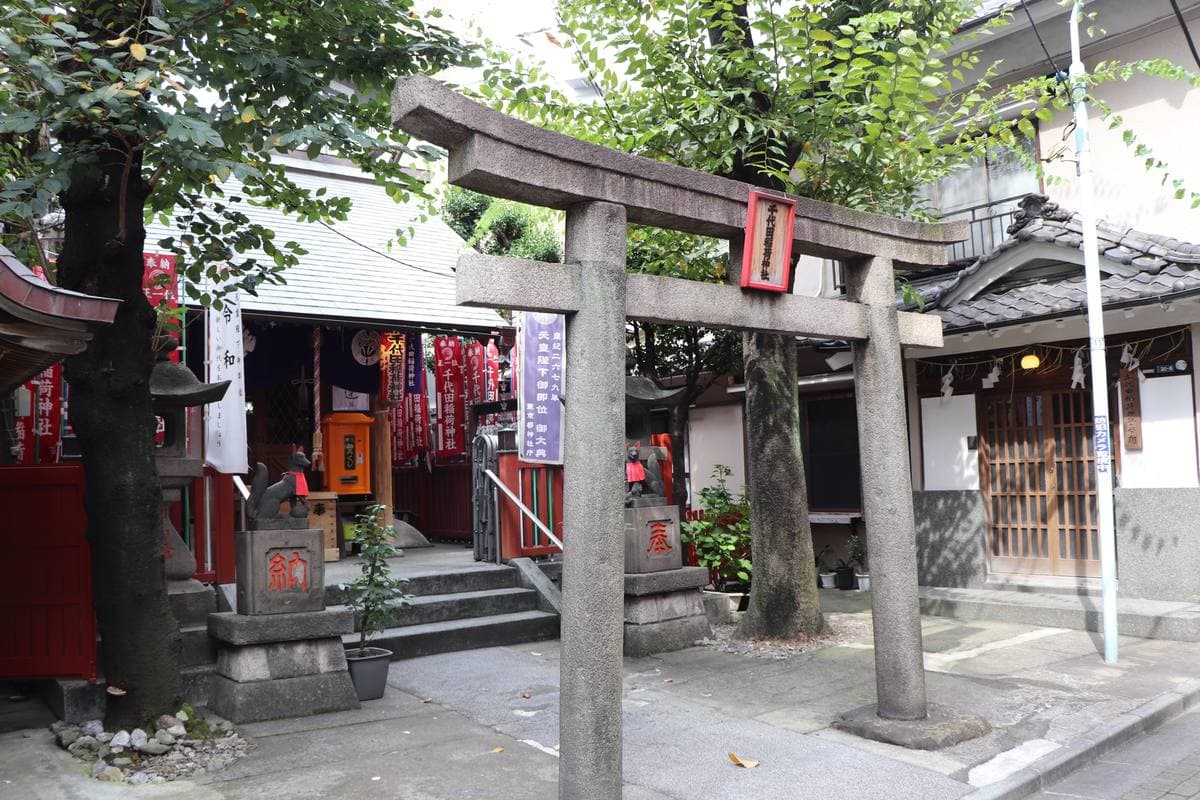 A stone torii and a small red shrine between shopfronts