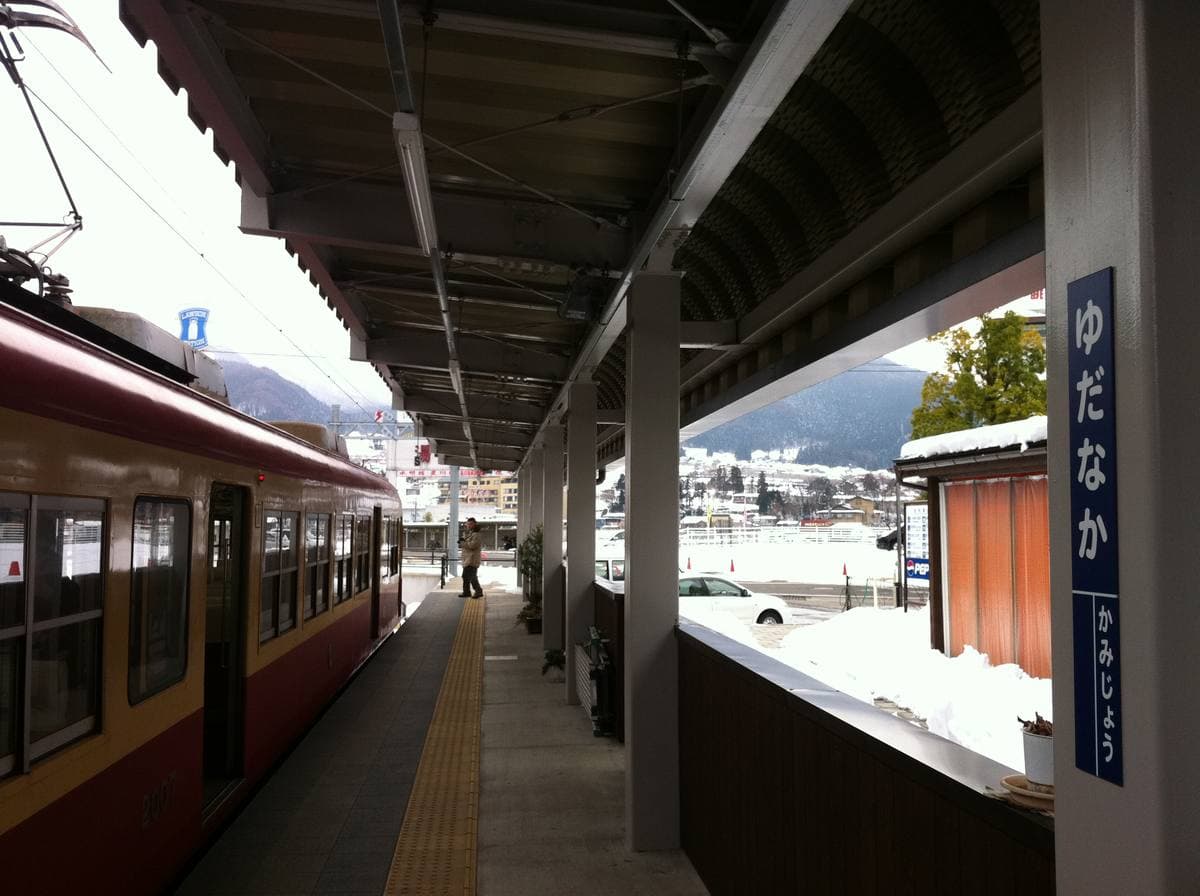 A red and white train at a small station, snow on the roofs