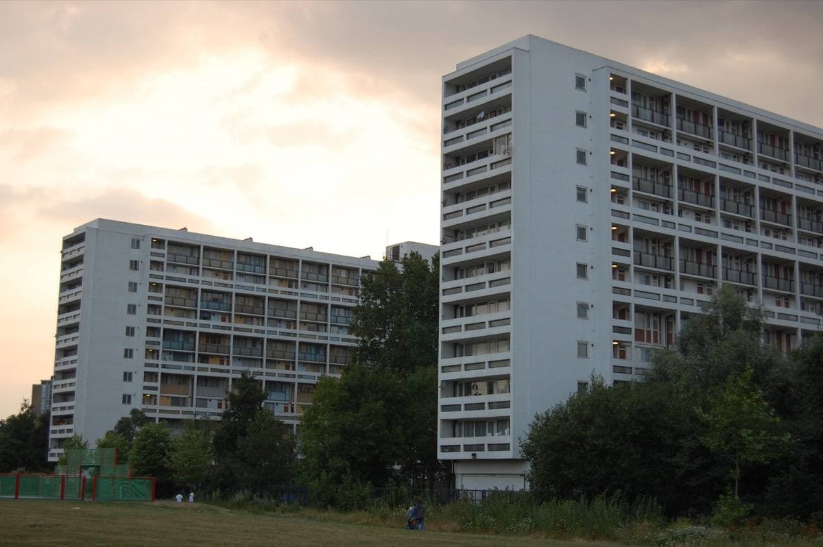 Two tall slab blocks of council flats against a pale sky, with trees in front
