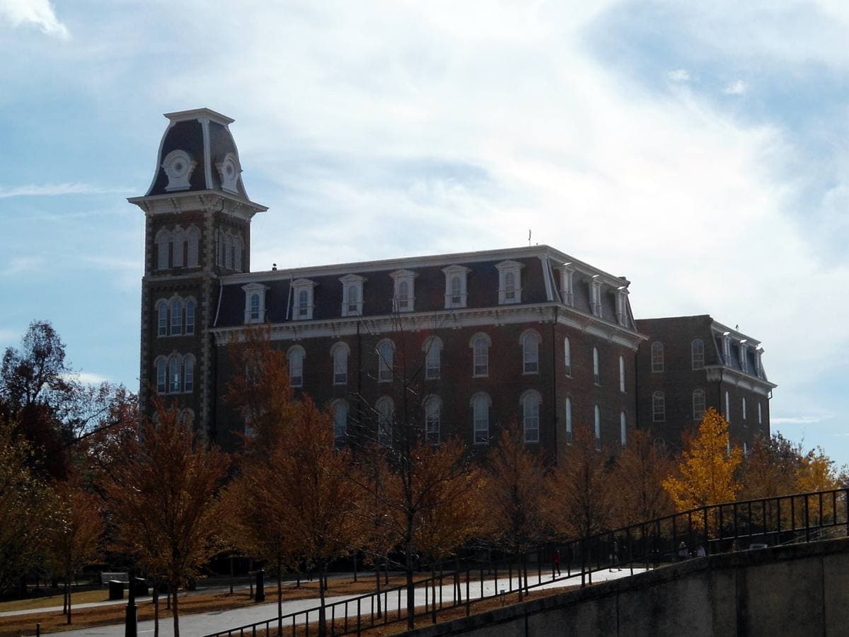 A Victorian brick hall with a tall tower behind autumn trees