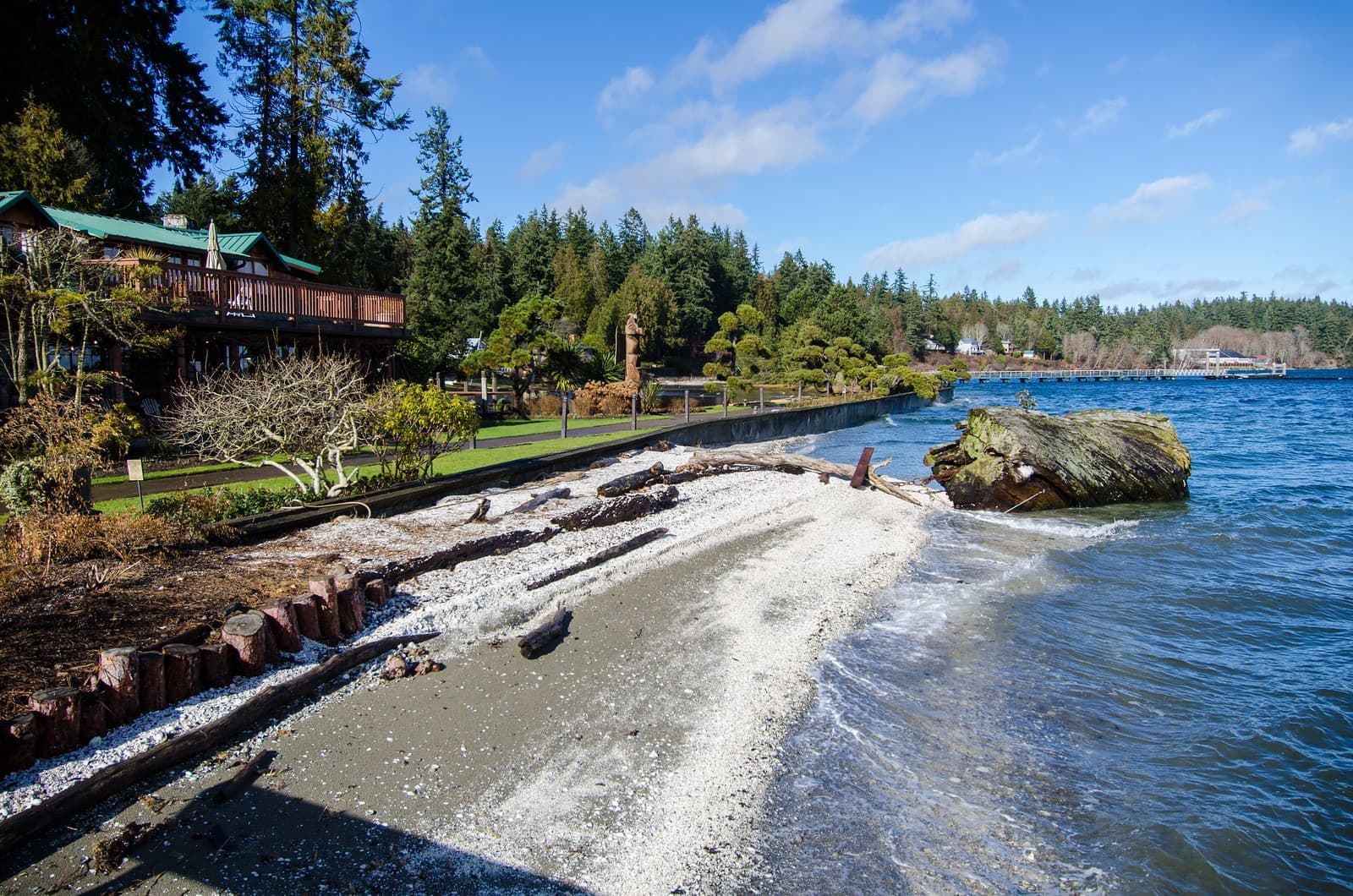 Kiana Lodge shoreline with a large log, lodge balcony, trees and blue water.