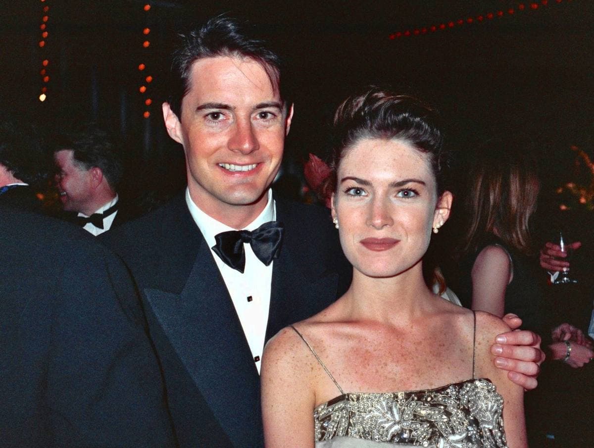 Kyle MacLachlan in a bow tie with his arm round Lara Flynn Boyle at a crowded evening party.