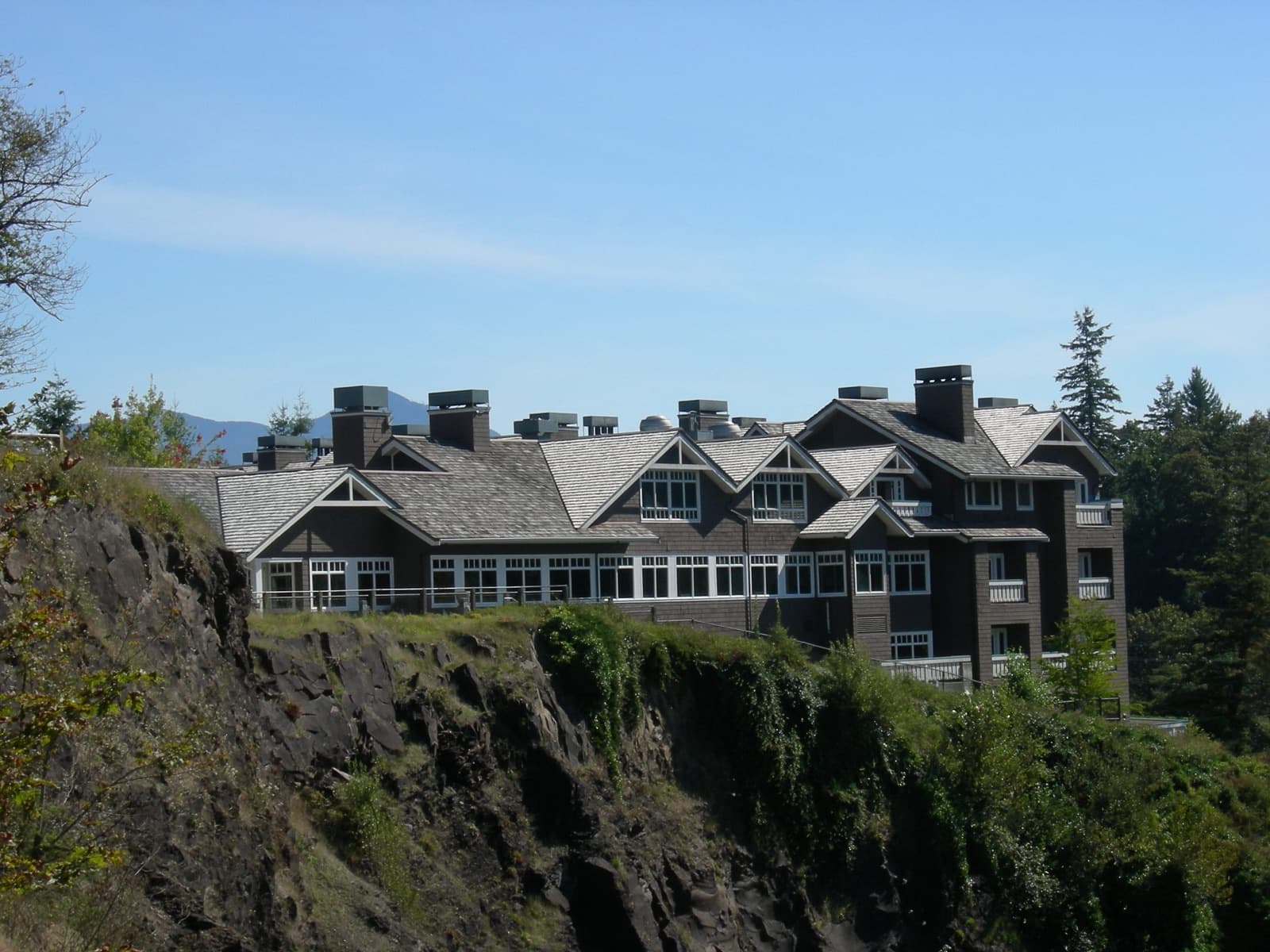 Salish Lodge rooflines and windows above a wooded rocky cliff beneath blue sky.