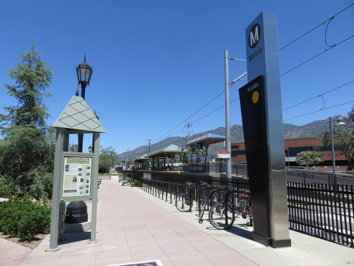 A light-rail platform with a lantern-topped kiosk under a blue sky, mountains beyond