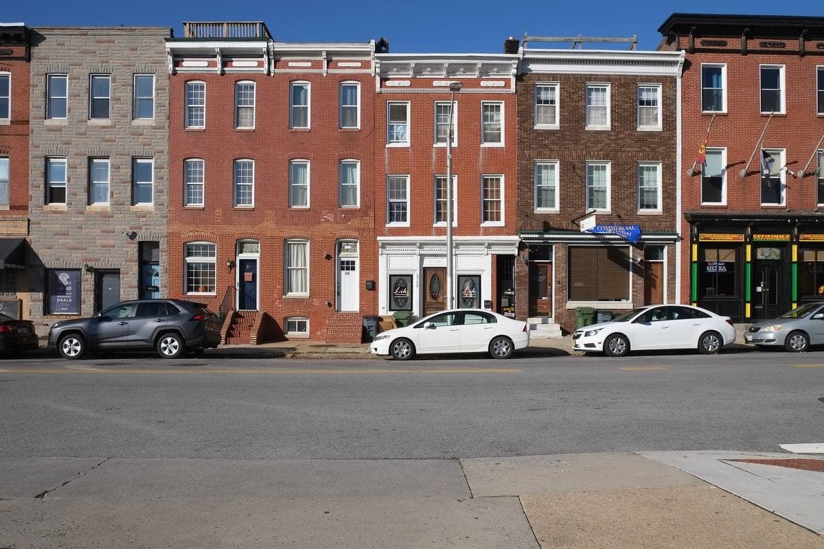 A row of brick rowhouses with parked cars along a wide street