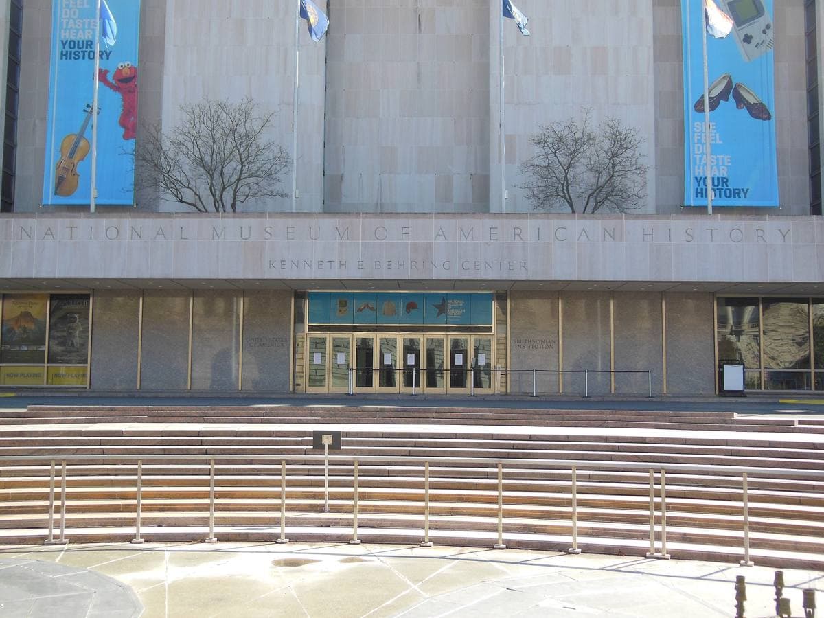 The long stone front of a museum with steps and a plaza along an avenue