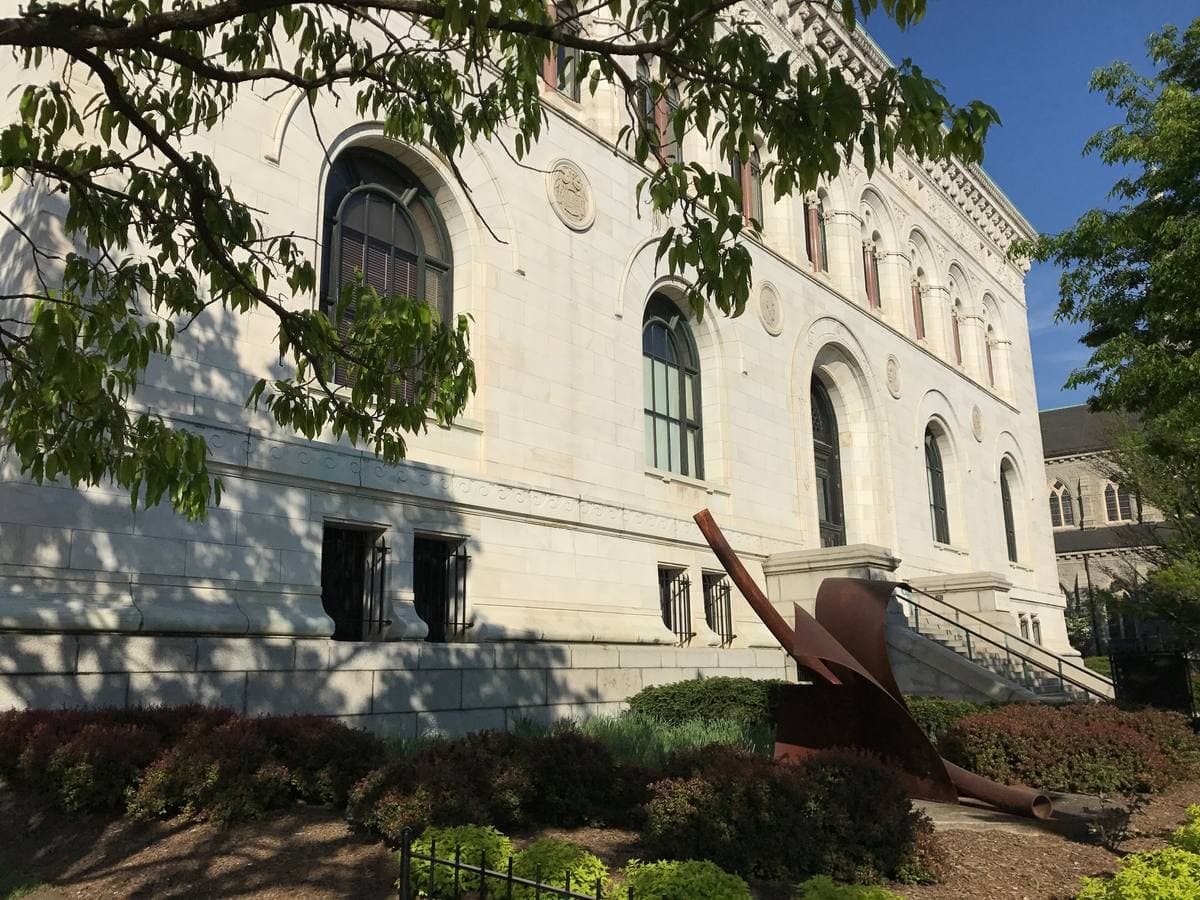 A white marble Renaissance-style building with arched windows behind trees, a flight of steps at its side