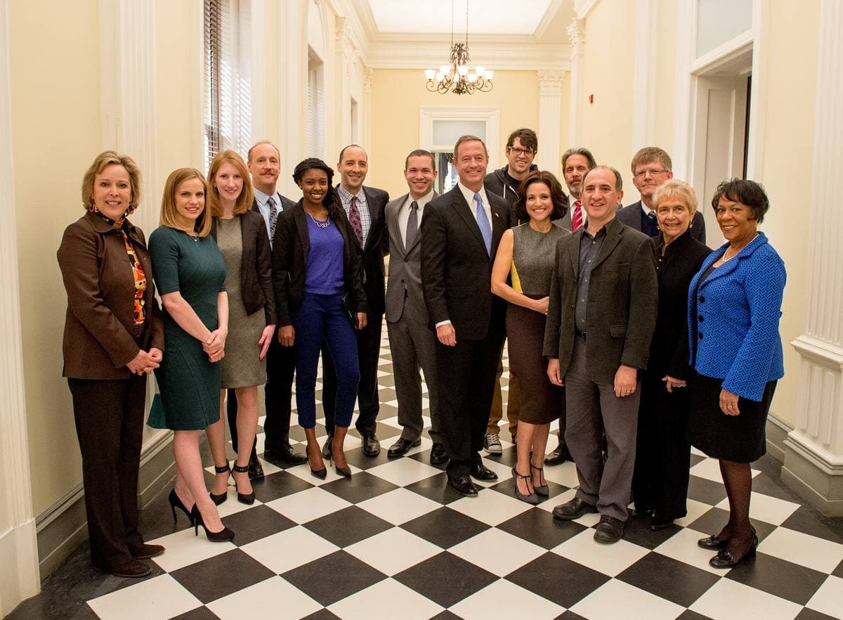A group of people posing in a corridor set with a black-and-white chequered floor and white panelled walls