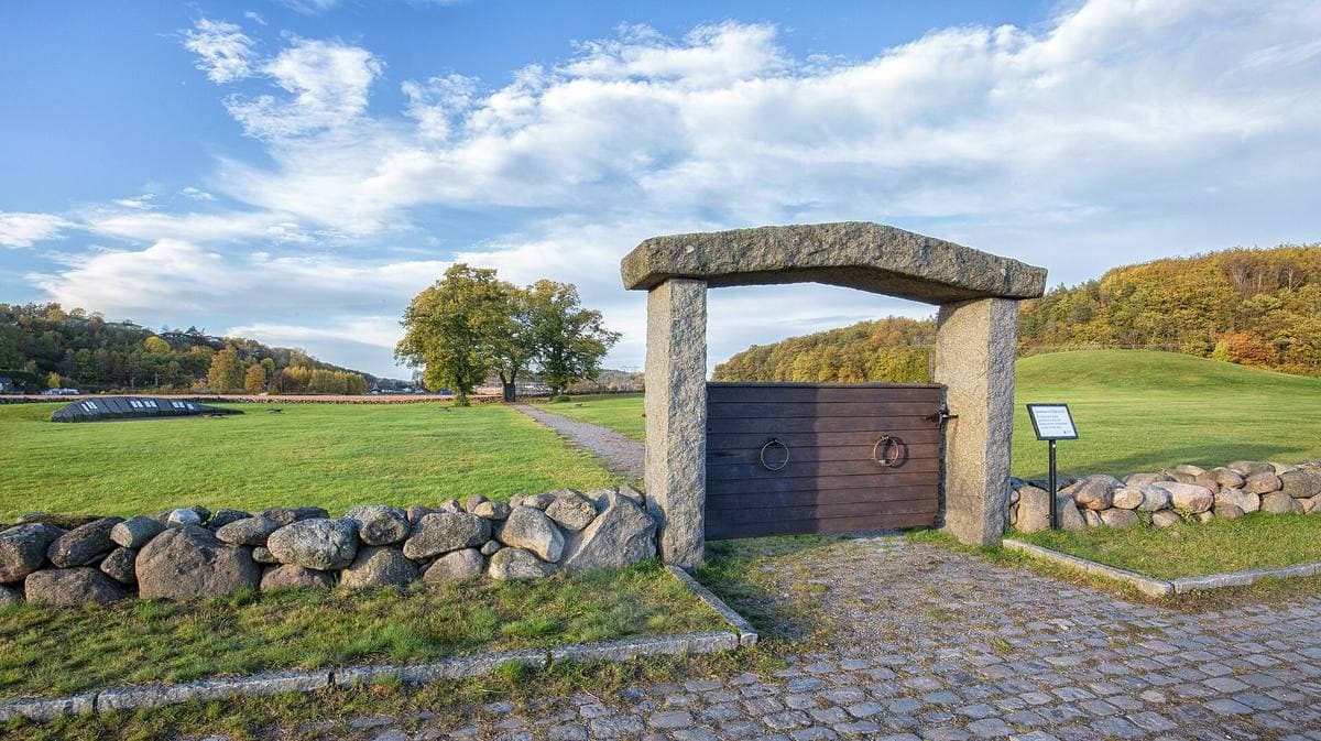 A grassy mound behind a stone gateway and a low stone wall