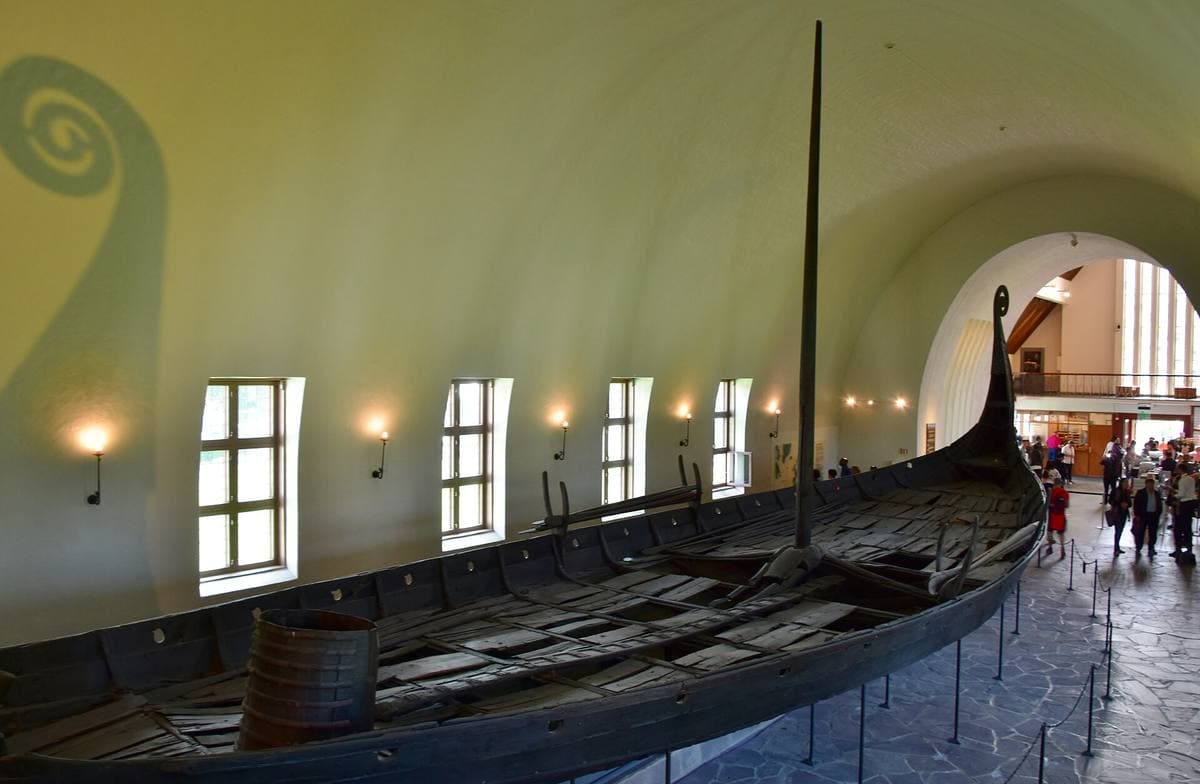 A long dark wooden ship on display in a white vaulted hall