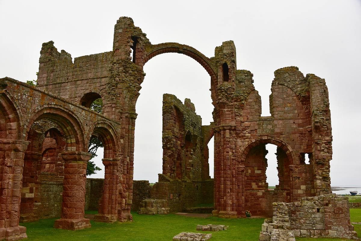 Red sandstone ruins with a tall arch against a pale sky