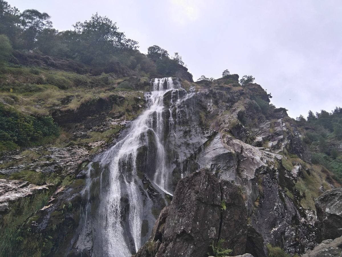A tall waterfall falling down a dark rock face among trees